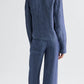 Person with back to camera wears the TWP Lucy Hemp Denim Top in blue—a loose, boxy silhouette with long sleeves—paired with wide-leg pants against a plain light background.