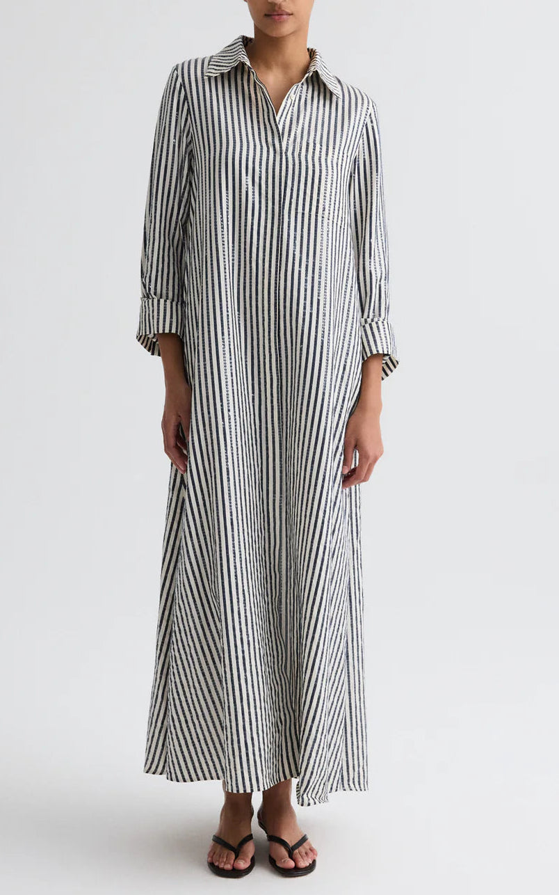 A person wears TWP's Jenny's Clear Sequin Stripe Gown, an oversized maxi dress with black and white stripes, a collar, and long sleeves, paired with black sandals.