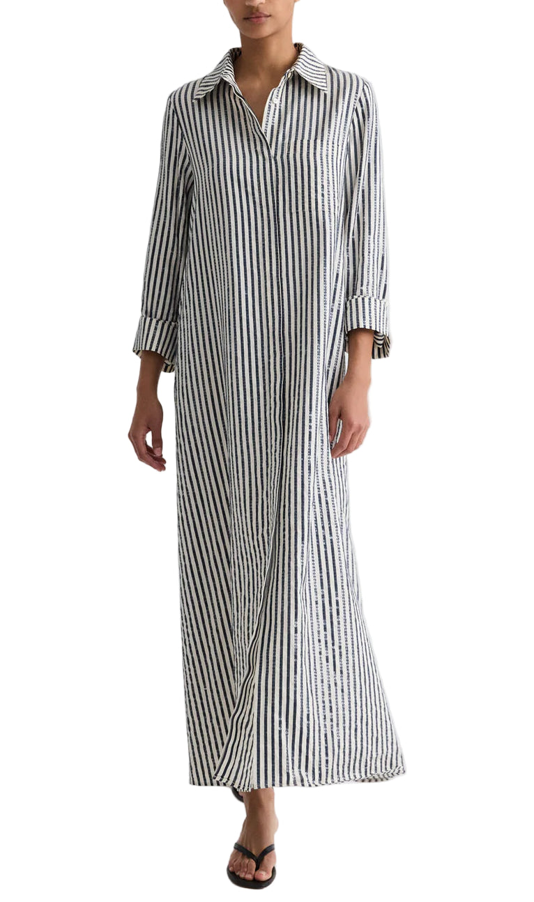 A person wearing the TWP Jenny's Clear Sequin Stripe Gown with vertical stripes, long sleeves, a collared neckline, and a button-up front, stylishly paired with black sandals.