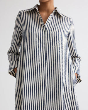 Person wearing TWP’s Jenny's Clear Sequin Stripe Gown, featuring vertical navy and white stripes and crafted from Italian cotton shirting, photographed from the shoulders down with hands in pockets.