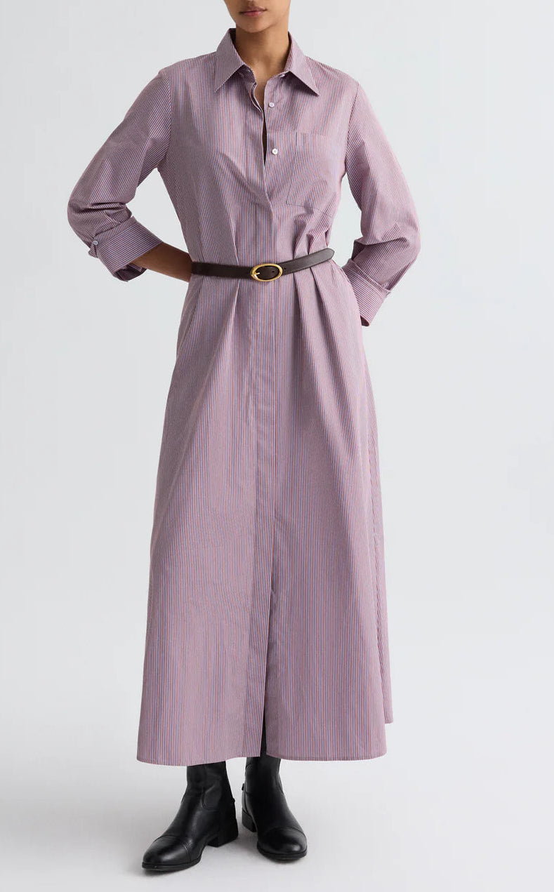 A person wearing TWP’s Jenny's Framed Micro Striped Gown with a black belt and black ankle boots stands against a plain light background.