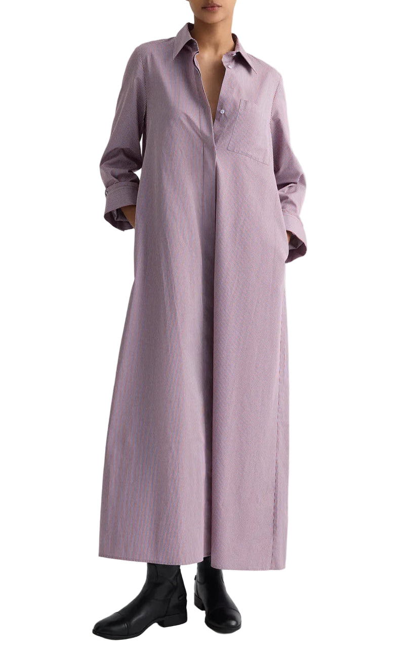 A person wears TWP's Jenny's Framed Micro Striped Gown—a long, loose-fitting, light purple striped maxi shirt dress with a collar and chest pocket—crafted from Italian cotton shirting, paired with black ankle boots.