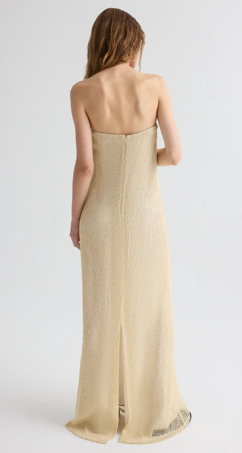 A woman faces away, wearing the TWP Carolyns Sequin Netting Gown—a strapless light gold maxi dress with textured fabric and a back center slit, making it an elegant pick for any formal evening event.
