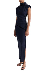 A person wears the TWP Gathered Thoughts Dress, a sleeveless navy blue maxi with high neckline and side slit, paired with black flip flops.