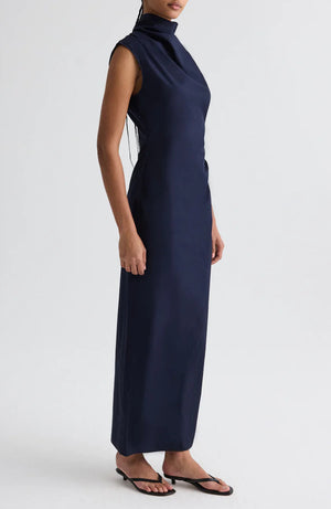 A model wears the TWP Gathered Thoughts Dress, a sleeveless navy blue maxi with a high neck, paired with black sandals, set against a plain white background.