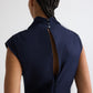 A person with braided hair wears the Gathered Thoughts Dress by TWP—a navy cap-sleeve dress with a back slit and two collar buttons, evoking the elegance of an open-back style.