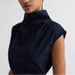 A person wears the Gathered Thoughts Dress by TWP, a sleeveless, high-neck navy blue stretch cotton piece, shown from the shoulders up against a plain background.