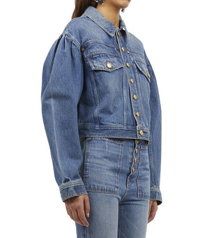 Person wearing an Ulla Johnson Cosette Jacket, a premium denim piece featuring puffed shoulders, button closures, and front pockets, paired with matching blue denim jeans.