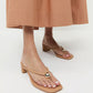A person wearing a tan midi skirt and Loeffler Randall’s Odessa Heeled Mule in beige nappa leather with a gold ball detail, standing on a white background.