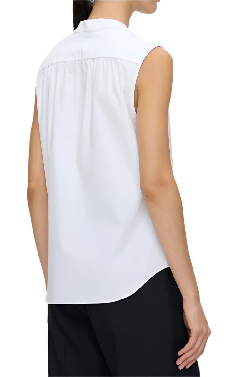 A person is wearing the Olympia Sleeveless Top by Callas Milano, a white blouse paired with black pants for modernist flair. Their neatly tied hair emphasizes the outfit as an essential wardrobe foundation.