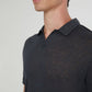 A man models the Onia Shaun Linen Polo, a dark linen jersey with a relaxed fit and split Johnny collar, shown from the shoulders up against a plain background.