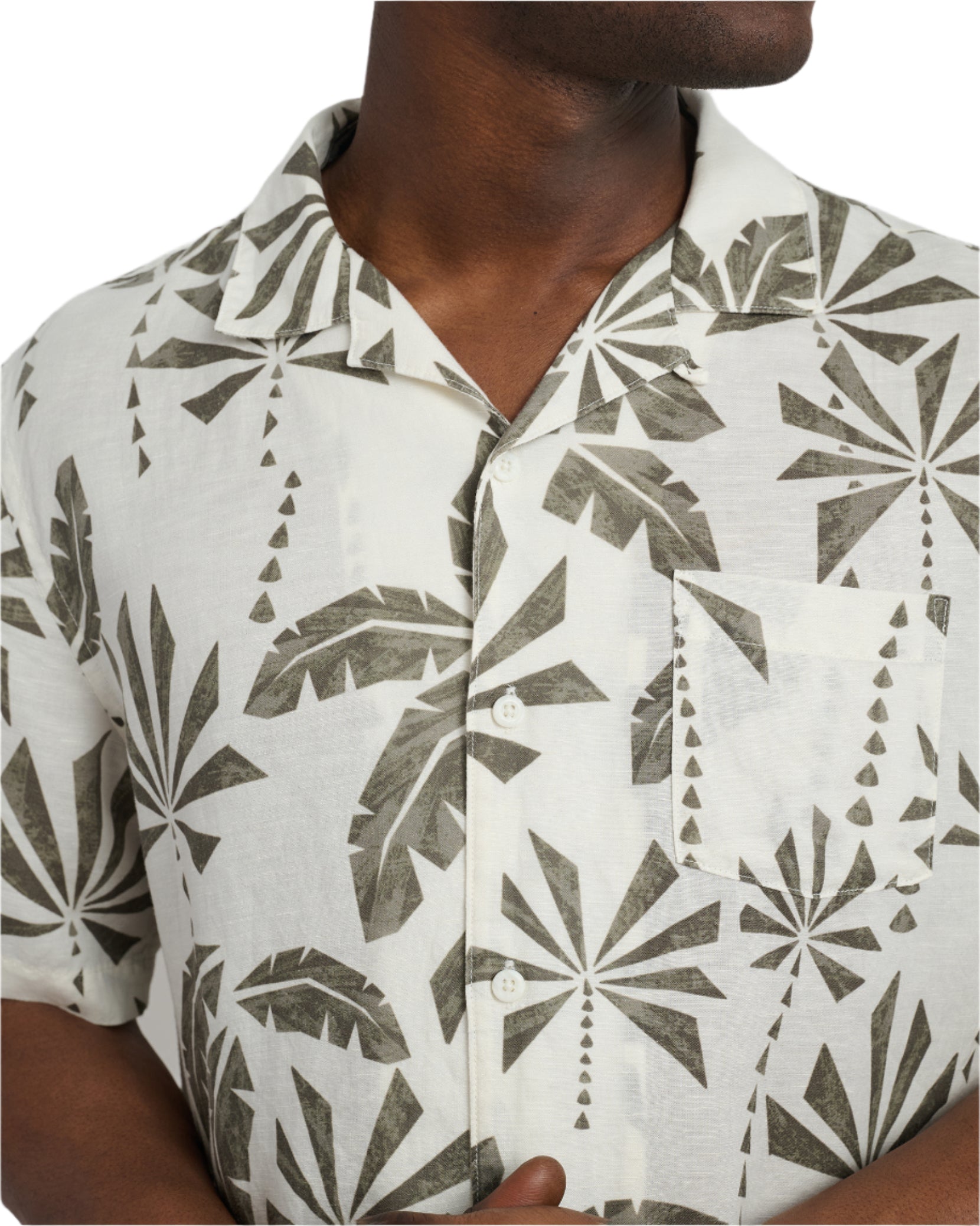 Someone is wearing the Onia Air Linen Vacation Shirt, a relaxed-fit white short-sleeve shirt with a green leaf pattern, made from breathable air linen fabric—perfect for vacation.
