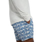 Someone wearing an Onia Charles 5" Swim Trunk and a white long-sleeve shirt stands with hands in pockets. The blue swim trunks feature a geometric design and quick-dry fabric, providing comfort and style all day.