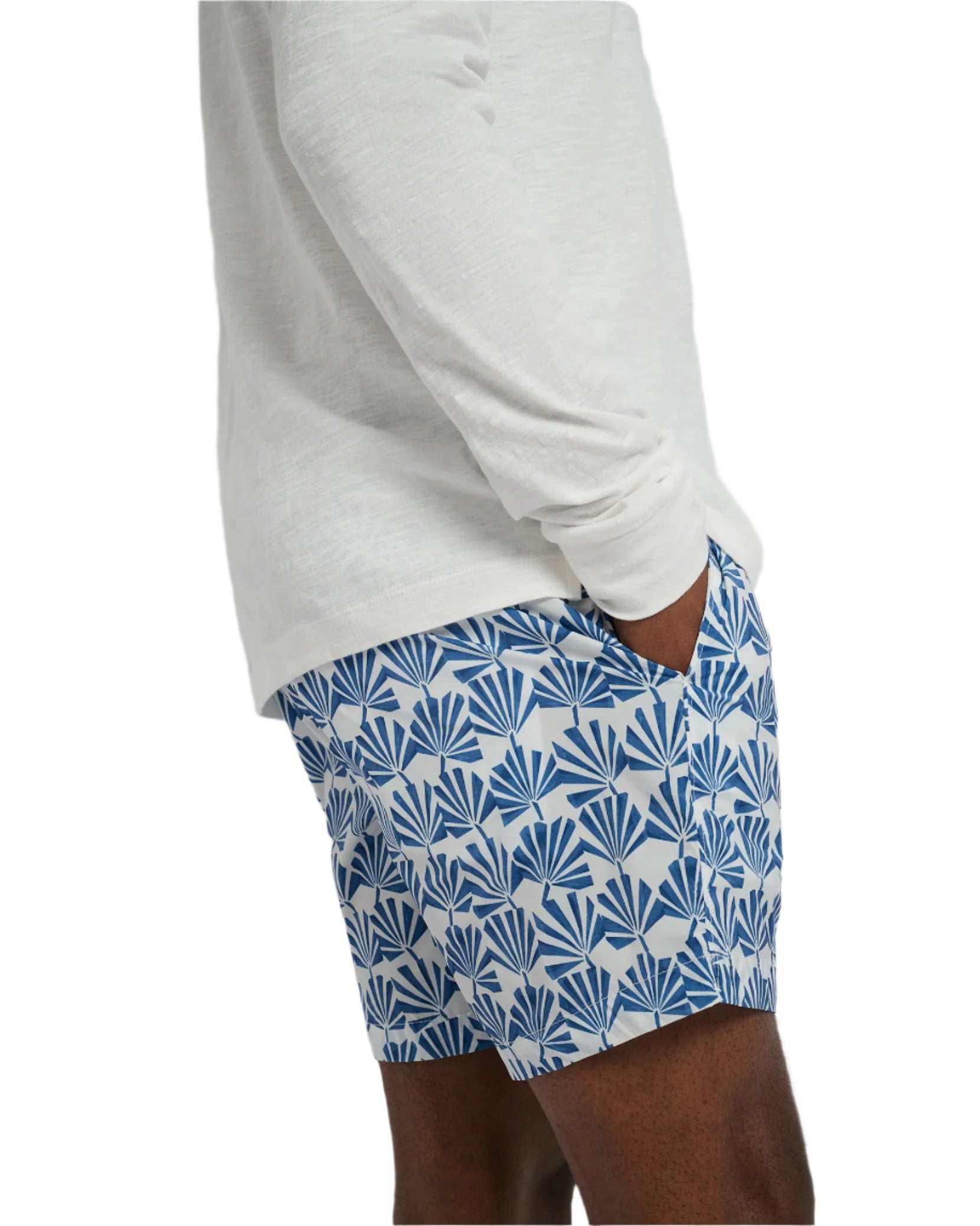 Someone wearing an Onia Charles 5" Swim Trunk and a white long-sleeve shirt stands with hands in pockets. The blue swim trunks feature a geometric design and quick-dry fabric, providing comfort and style all day.