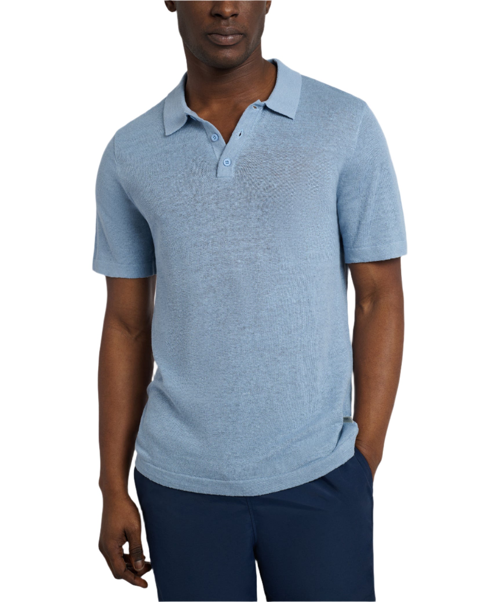 Standing against a white background, they wear Onia's Linen Sweater Polo in light blue with dark blue pants, one hand in the pocket. The outfit offers a relaxed fit ideal for any casual outing.