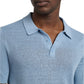 A man models the Onia Linen Sweater Polo, featuring a light blue, relaxed fit and short sleeves. It's crafted from linen jersey knit and showcased against a plain white background.