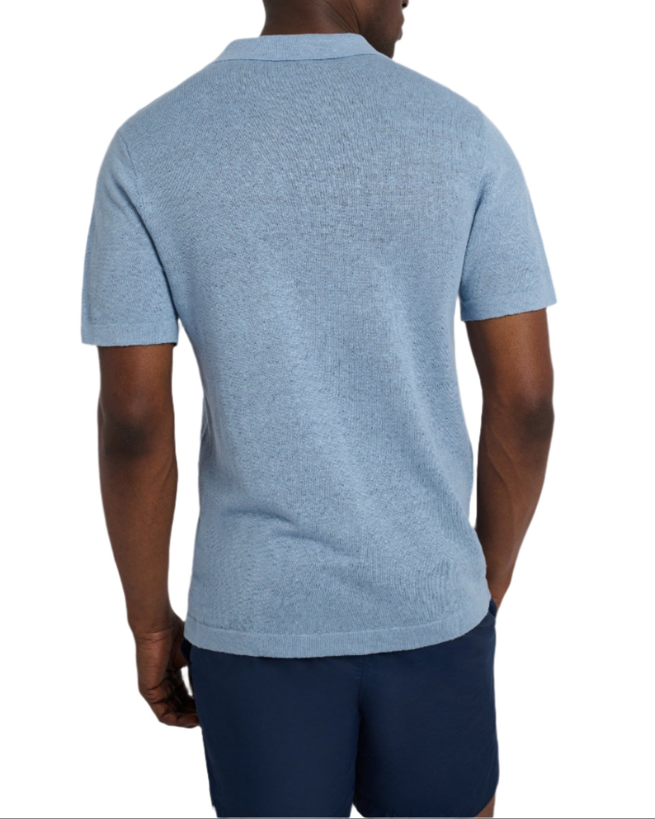 An individual wearing a relaxed fit, light blue Onia Linen Sweater Polo and navy shorts is standing with their back to the camera.