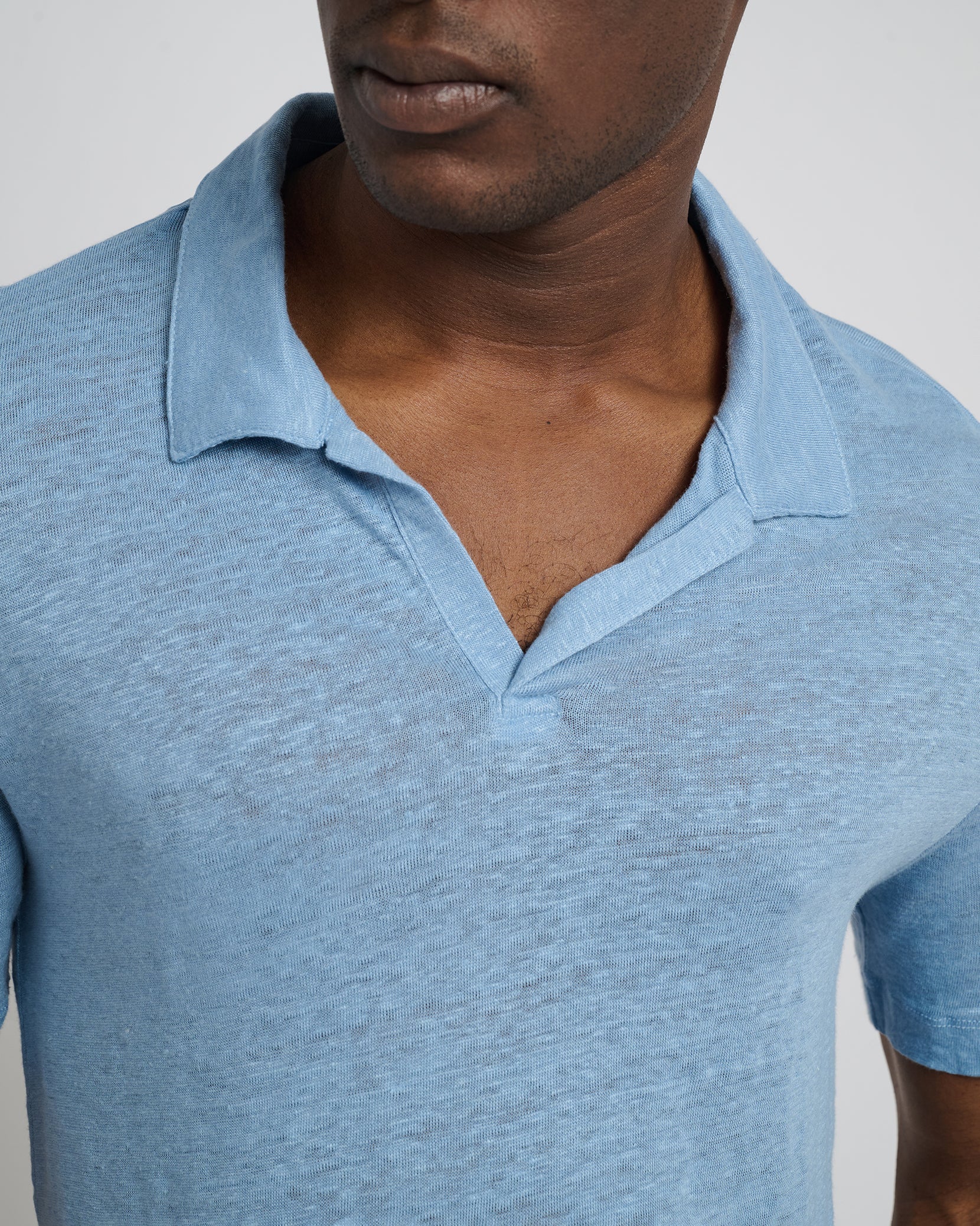 Someone wears the Onia Shaun Linen Polo in light blue, featuring a relaxed fit and Johnny collar, shown from shoulders to upper chest, facing slightly to the side.