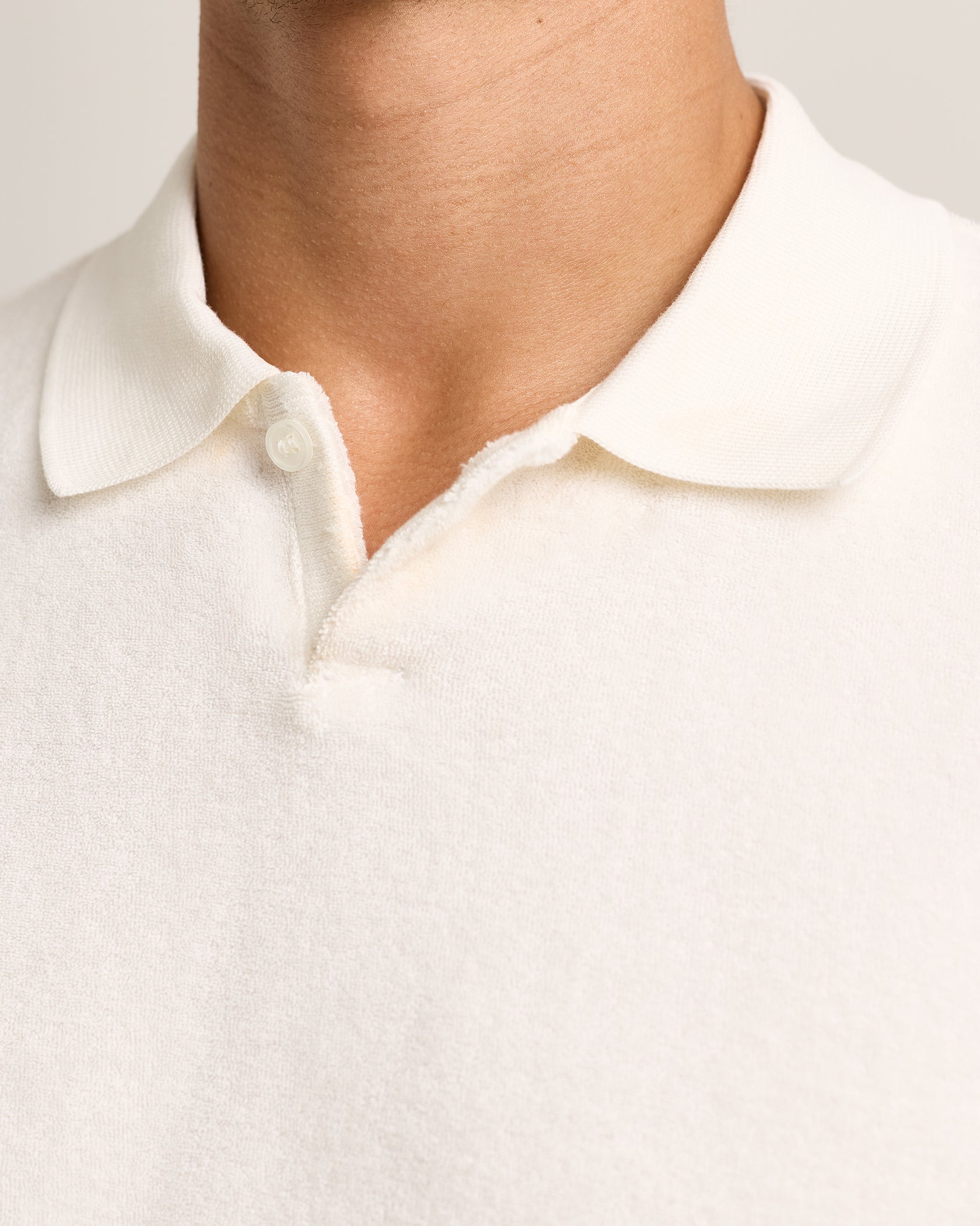 Close-up of a person wearing the Orlebar Brown Bruno Towelling Polo in white, highlighting the neck and upper chest area.