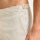 Close-up of a person wearing Orlebar Brown Bulldog Classic Stripe Shorts, featuring cream-colored vertical stripes, signature side-fasteners, and a visible tag near the waistband.