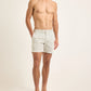 A man stands against a plain background wearing Orlebar Brown Bulldog Classic Stripe Shorts—light, quick-drying tailored swim trunks—and dark sandals, with hands in pockets and no shirt.