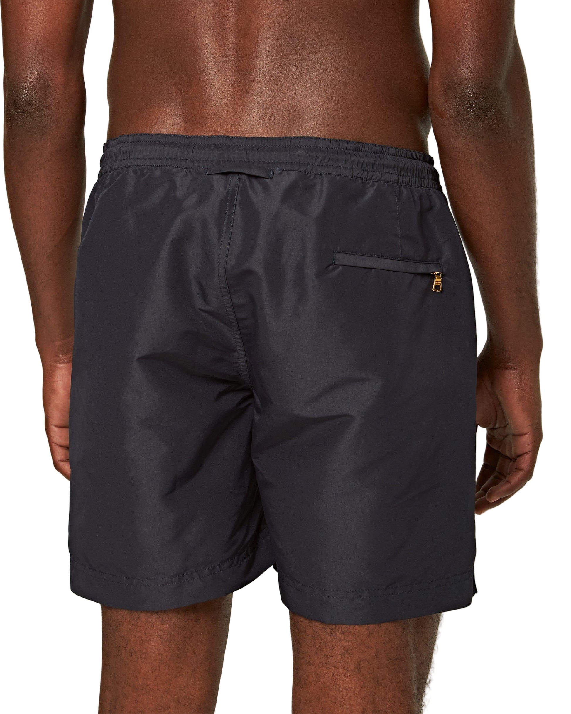 A person is shown from behind wearing Orlebar Brown Bulldog Drawcord Shorts in black, which feature an elastic waistband and a zippered back pocket.