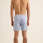 A man stands barefoot with his back to the camera, wearing Orlebar Brown Bulldog Drawcord Seersucker Shorts in light blue against a plain background.