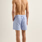 A man faces away from the camera against a plain background, wearing Orlebar Brown Bulldog Drawcord Swim Shorts in light blue with a rope-style drawcord and no shirt.