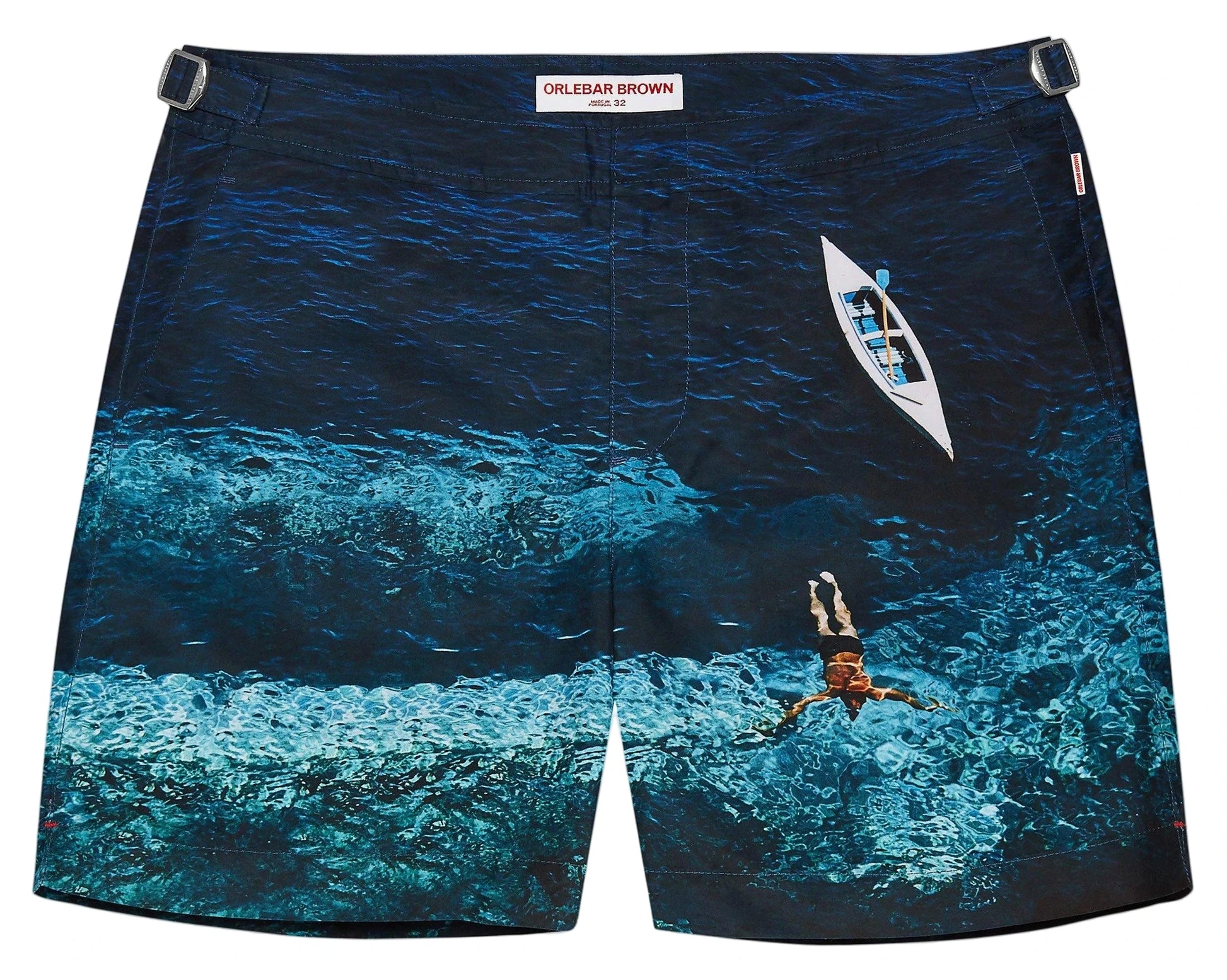 Orlebar Brown Bulldog Photographic Swim Trunks feature a tailored fit and a printed aerial image of a person swimming in the ocean beside a small boat.