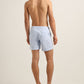 A man faces away from the camera, wearing Orlebar Brown Bulldog Swim Shorts in Surfside Blue and black slide sandals, set against a neutral background.