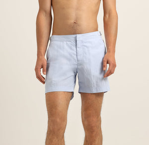A man models Orlebar Brown Bulldog Swim Shorts in Surfside Blue, standing bare-chested with his hands by his sides against a plain light background.
