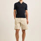 Wearing the Orlebar Brown Keeling 3 Button Polo in understated navy, paired with refined beige knee-length shorts, a person stands against a plain light background, evoking the deep elegance of Night Iris.