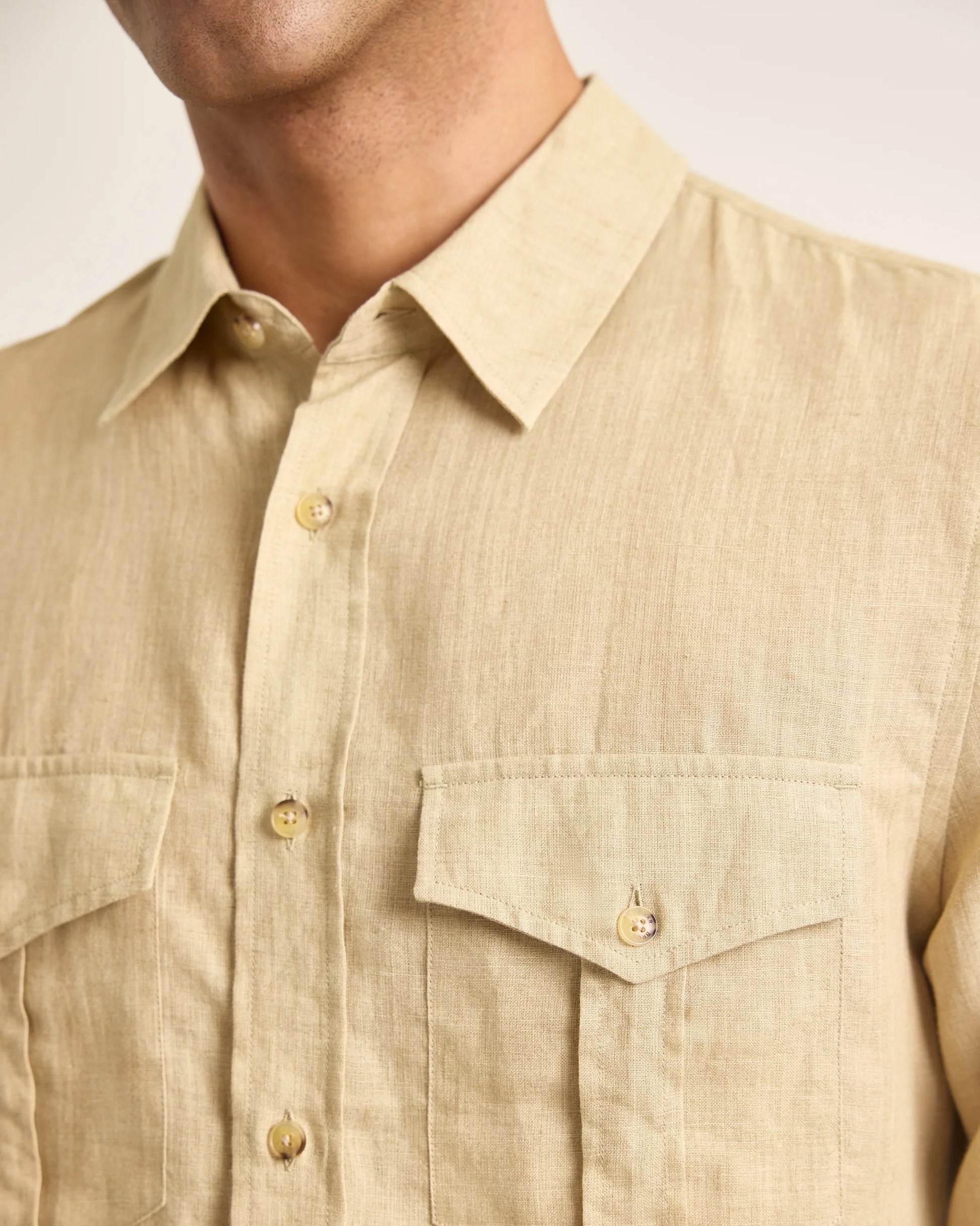 A close-up of a person wearing the Orlebar Brown Colburn Lino Shirt, a beige linen button-up featuring two chest pockets and a pointed collar.