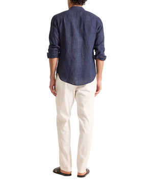 A person stands facing away, wearing the Orlebar Brown Colburn Lino Shirt in navy, paired with off-white pants and black sandals, against a plain white background.