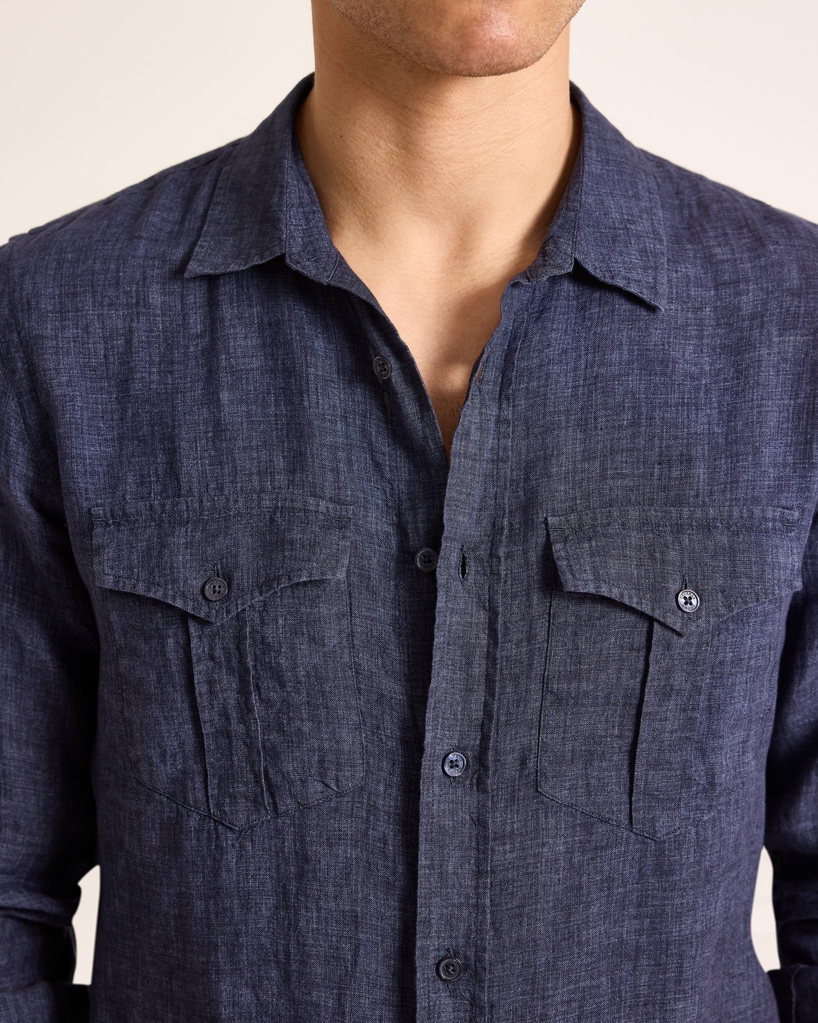 A person is wearing the Orlebar Brown Colburn Lino Shirt—a dark blue, tailored long-sleeve linen shirt with two chest pockets—shown in a photo from shoulders to mid-torso.