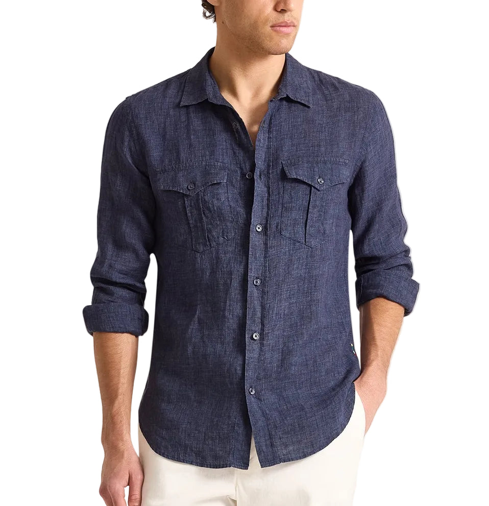 Man wearing the Orlebar Brown Colburn Lino Shirt, a tailored dark blue Italian linen button-up with front pockets, paired with white pants and standing against a plain white background.
