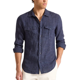 Man wearing the Orlebar Brown Colburn Lino Shirt, a tailored dark blue Italian linen button-up with front pockets, paired with white pants and standing against a plain white background.