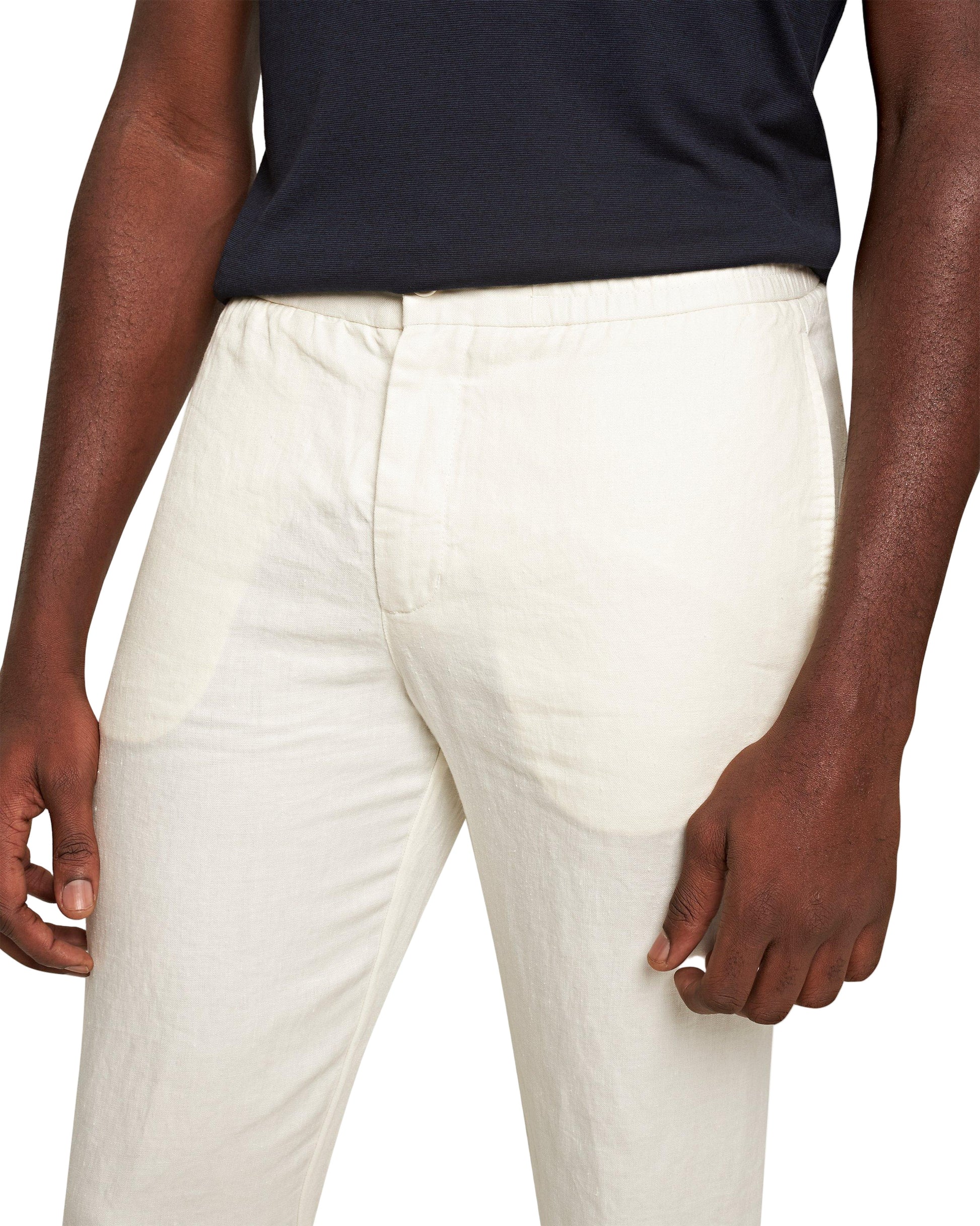 A person wearing Orlebar Brown's off-white Cornell Linen Trousers with a drawcord waistband and a black shirt, shown from waist to mid-thigh with arms relaxed at their sides.