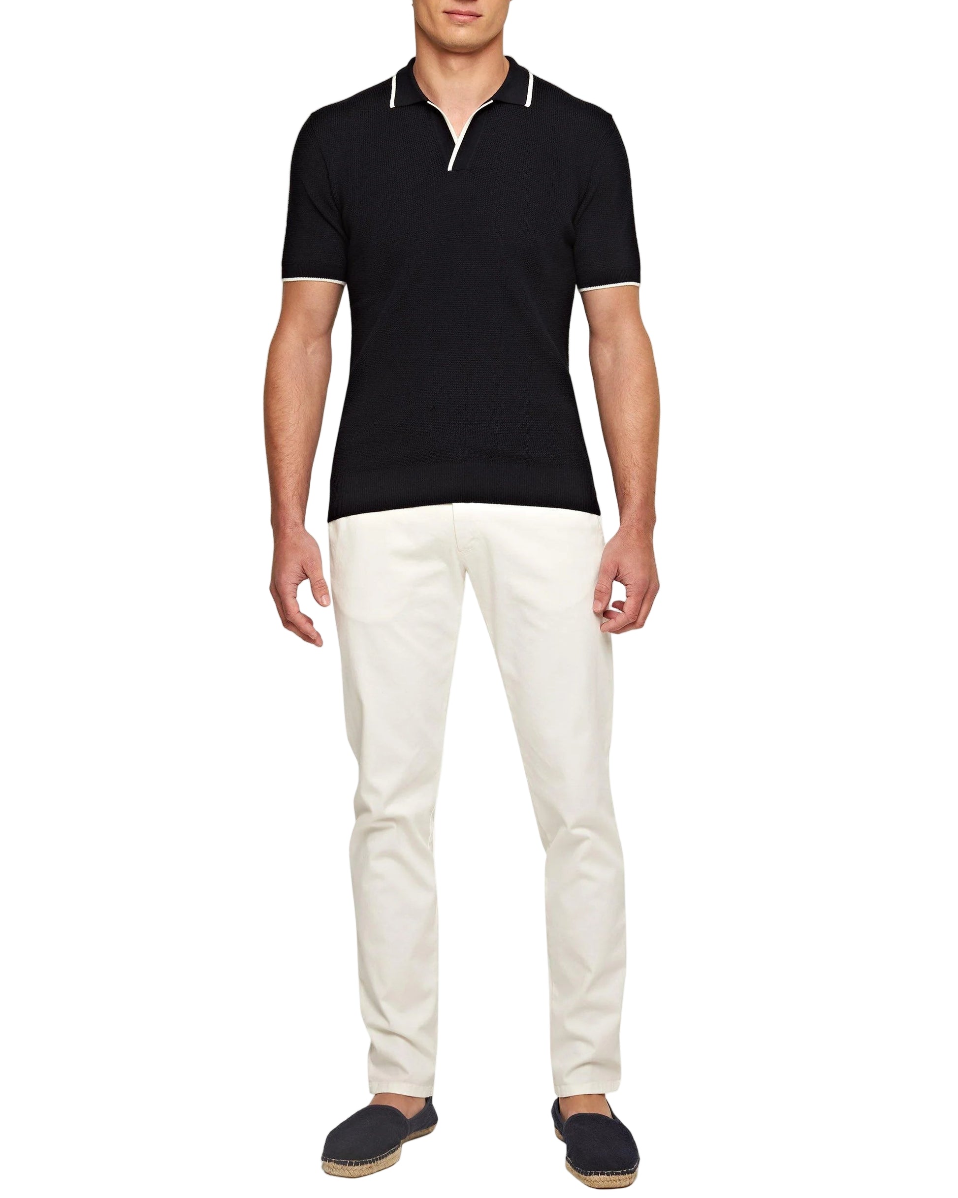 A man stands against a plain white background wearing a black short-sleeve polo shirt, Orlebar Brown Fallon Stretch-Cotton Pant, and dark slip-on shoes.
