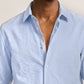 A person wearing the Orlebar Brown Justin Seersucker Stripe shirt, its light blue stripes perfect for summer, with the top buttons undone. Only the upper torso and neck are visible.