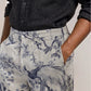 Wearing the Orlebar Brown Laurent Linen Zephra—a black button-up shirt paired with high-waisted linen pants featuring a blue floral and bird print—one hand casually in their pocket, this look makes an ideal choice for warm-weather dressing.