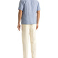 A man stands facing away, wearing the Orlebar Brown Maitan Lino Stripe Shirt with a relaxed fit and Capri collar, paired with off-white pants and black sandals against a white background.