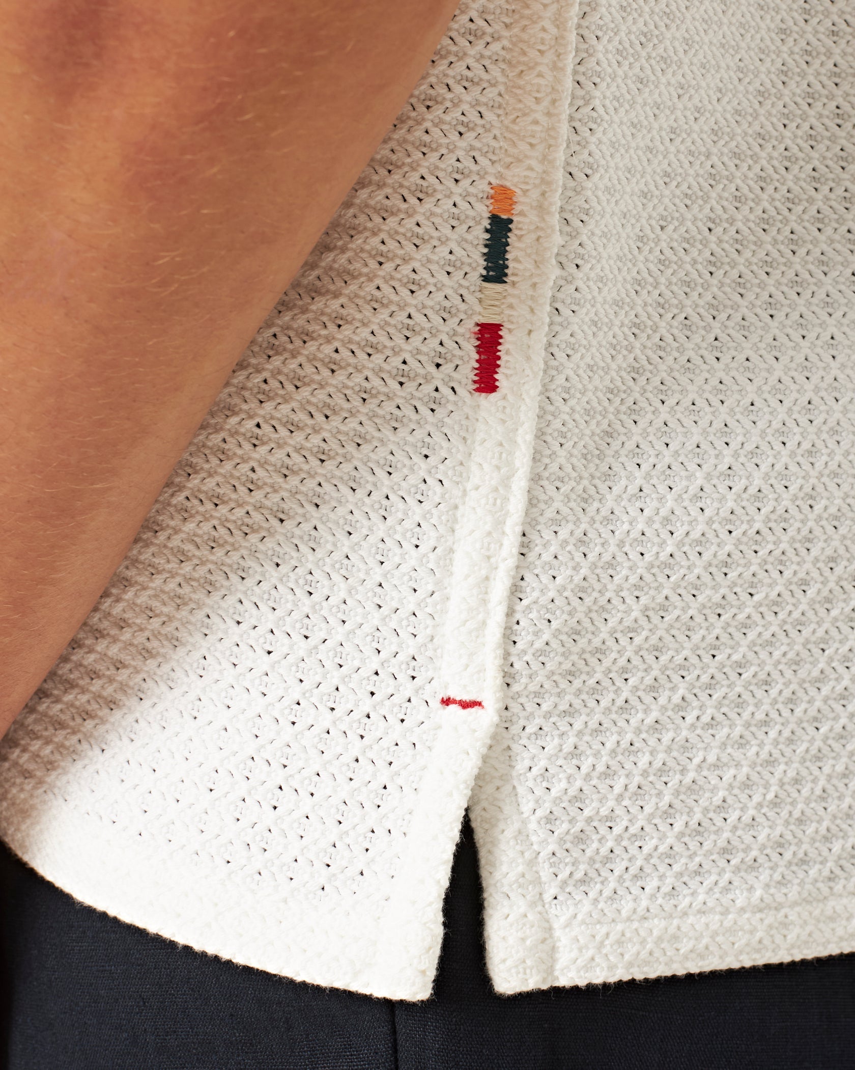 Close-up of the Orlebar Brown Maitan Open Weave Shirt with a Capri collar and side slit, featuring small multicolored stitched accents near the edge, paired with black pants.