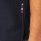 Close-up of a person's arm next to Orlebar Brown's Maitan Seersucker Woven Shirt in dark textured Italian cotton, featuring four small horizontal stitches in green, yellow, white, and red; patterned fabric visible at the bottom.