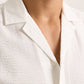 Close-up of a person wearing the Orlebar Brown Maitan Seersucker Woven Shirt, featuring white cotton fabric, a relaxed fit, and an open Capri collar that reveals part of their neck and chest.