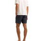 A man faces away, wearing the Orlebar Brown Maitan Seersucker Woven Shirt in white, paired with navy patterned shorts and black sandals, set against a white background.