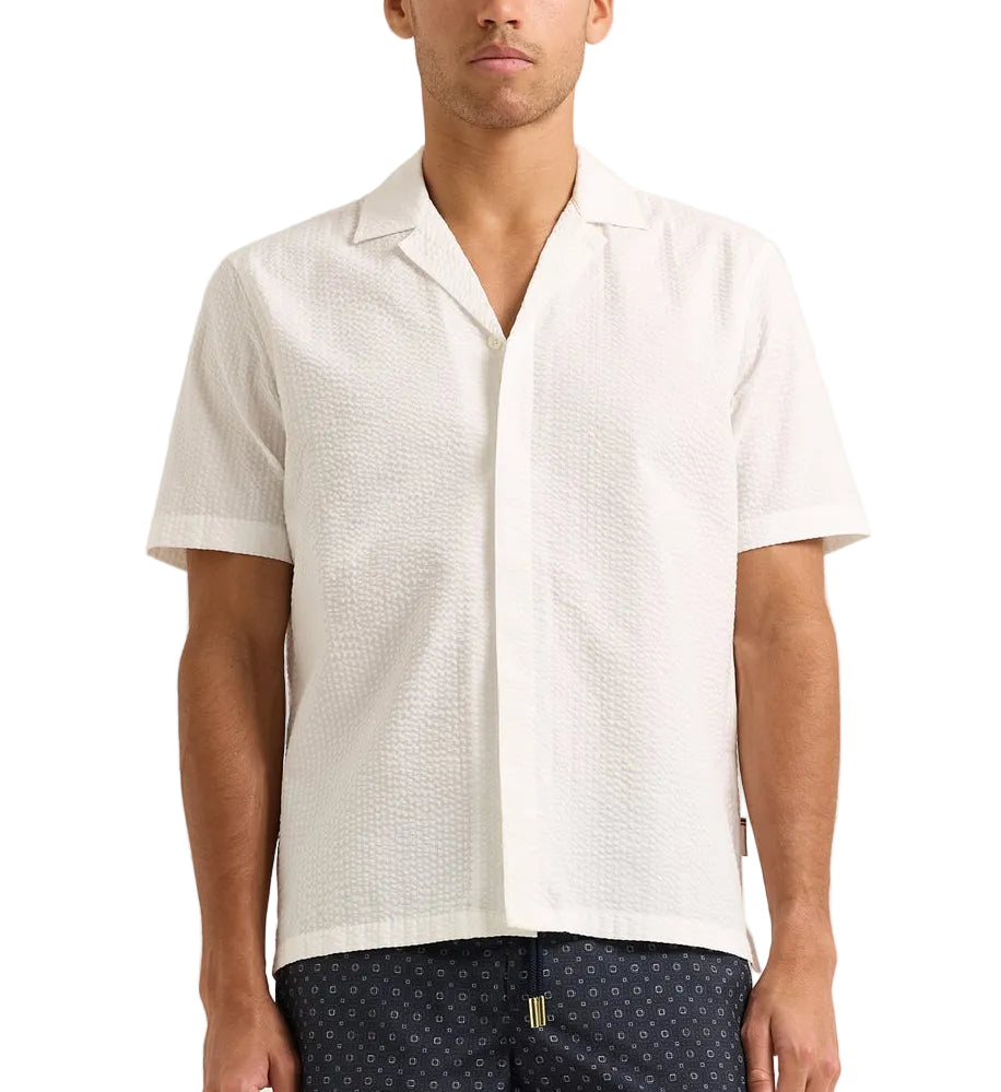 A man wearing the Orlebar Brown Maitan Seersucker Woven Shirt with a Capri collar and textured pattern stands against a plain background.