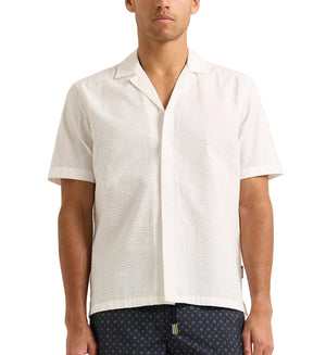 A man wearing the Orlebar Brown Maitan Seersucker Woven Shirt with a Capri collar and textured pattern stands against a plain background.