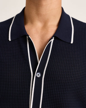 Close-up of a person wearing the Orlebar Brown Roddy Button Through Knitted Shirt in navy with textured waffle mesh and white piping—ideal for effortless summer tailoring.