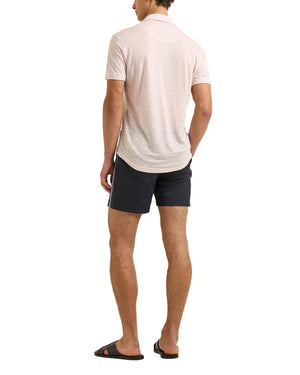 A man stands with his back to the camera, wearing a light pink Orlebar Brown Sebastian Linen Polo with a tailored fit, paired with dark shorts and black slide sandals against a white background.